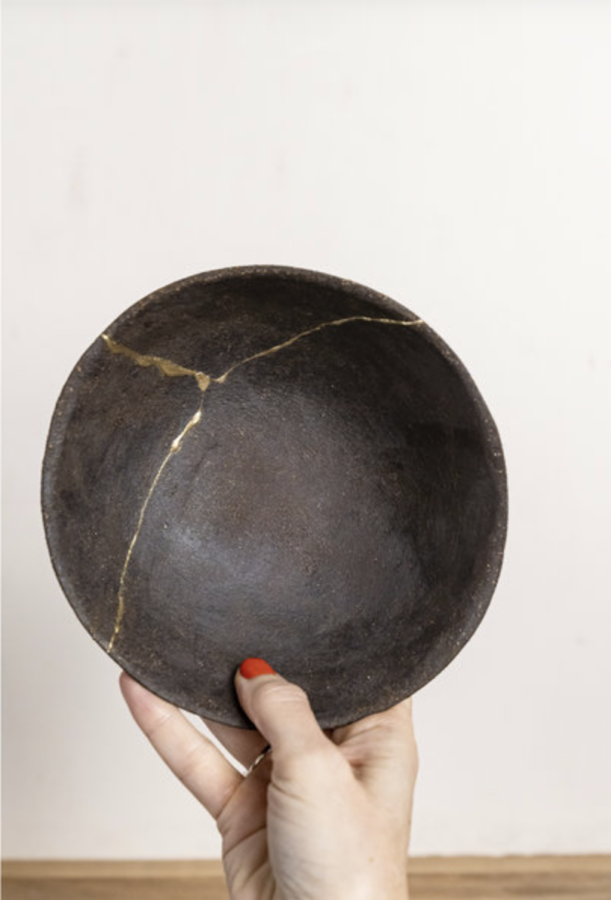 Gray bowl being held up by a woman's hand that has been repaired using the Kintsugi technique